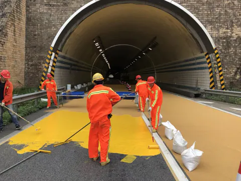Crew applying yellow colored anti-skid pavement coating at a tunnel entrance